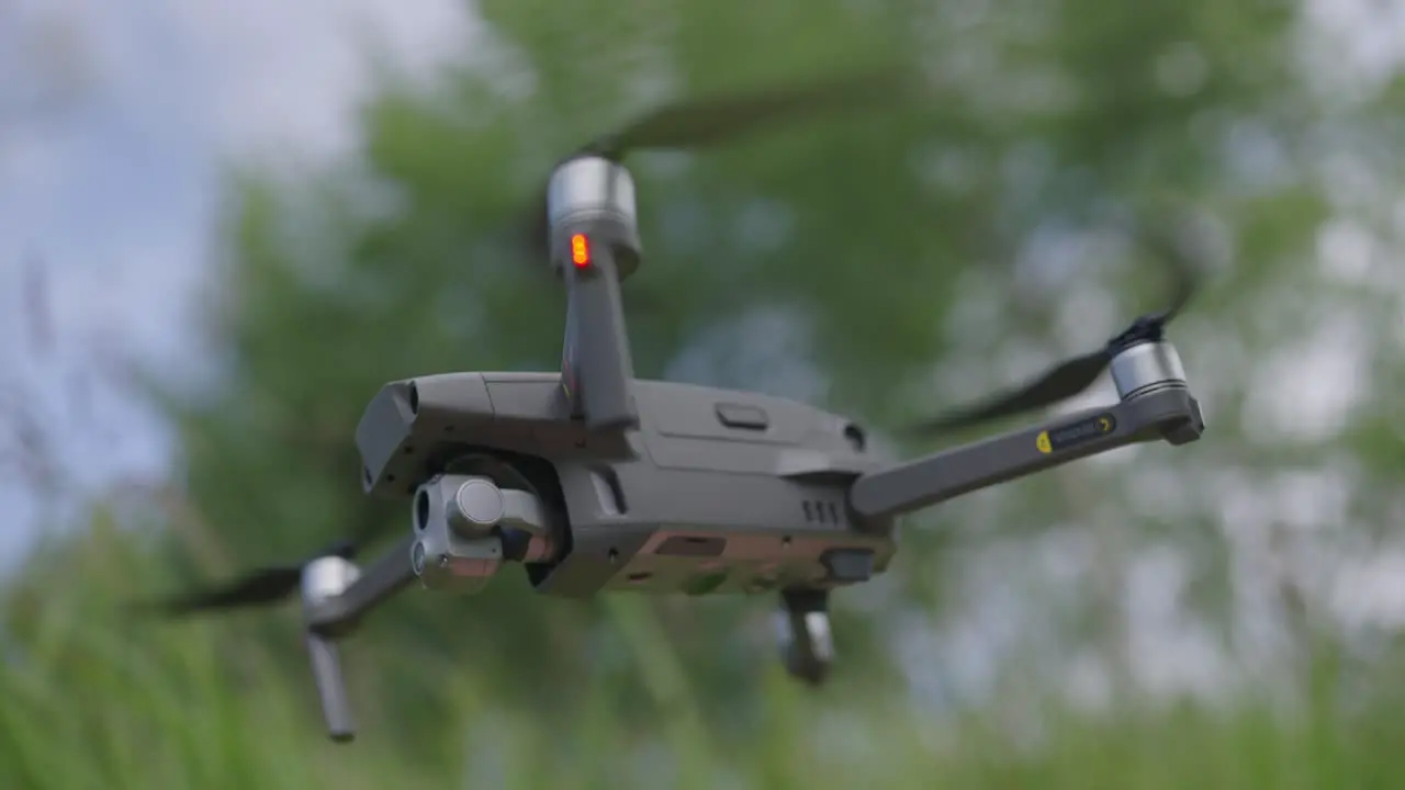 Close up shot of a hovering drone from a low angle with trees and grasses in the background