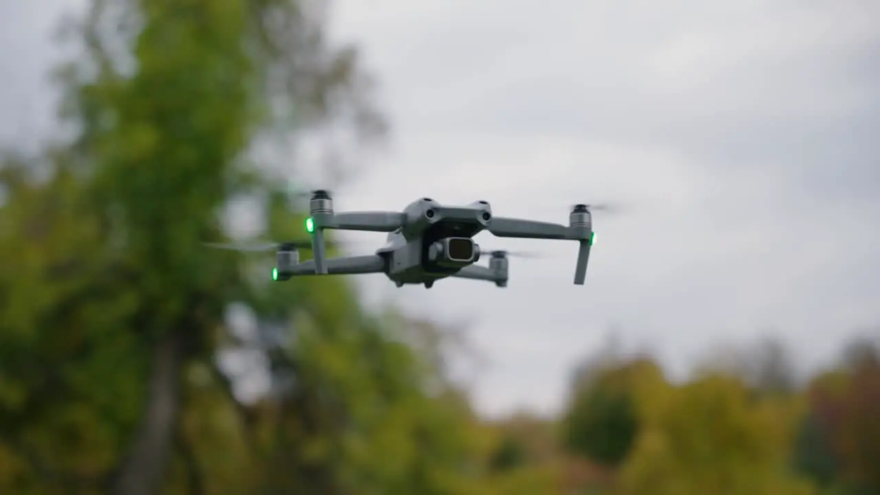 orbital shot of a dji drone flying in mid air with trees in the background