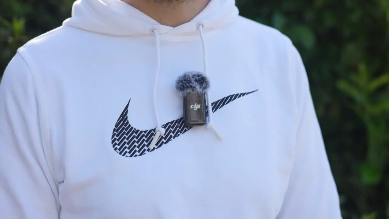 Hand Turning On DJI MIC Attached To White Sports Hoody With Deadcat On Top