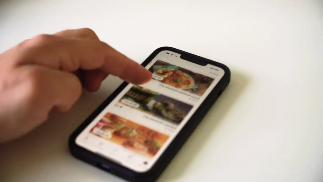 the shot of man's hand scrolling the food ordering app on a smart phone to pick the food for dinner