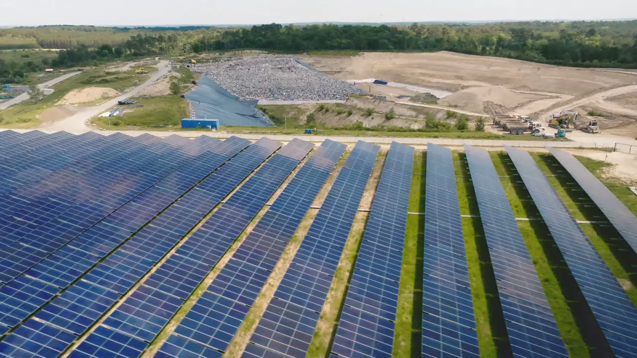 Forward motion in solar panels seen from a drone with a landfill in the background trucks transporting waste to landfill