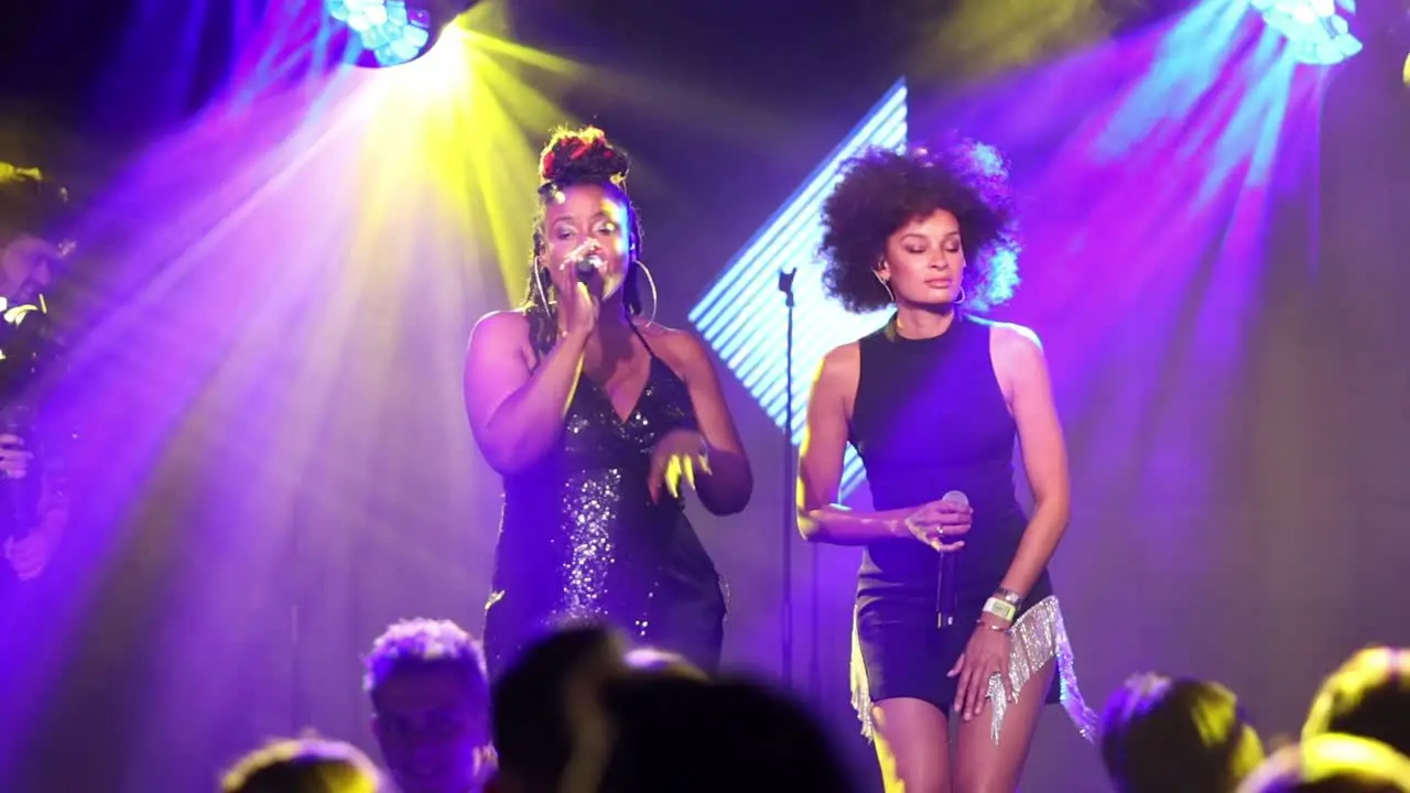 BBC Singer Kelly Jade Williams performs on stage in a nightclub with a co-singer with a videographer filming in the background slow motion