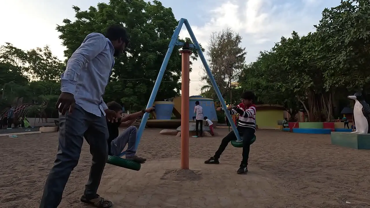 A father amuses his two children by spinning them on a ride in a public park