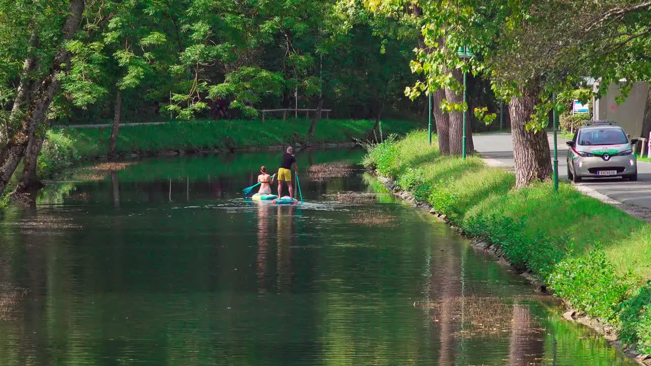 A man and a woman on stand up paddles on the water in a canal