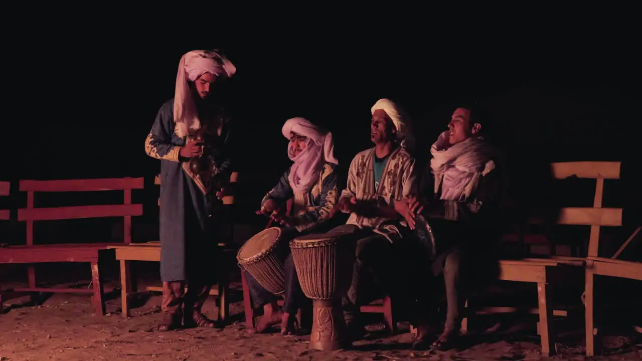 Berber nomad people gathered around a campfire in Morocco playing music and singing in the desert night