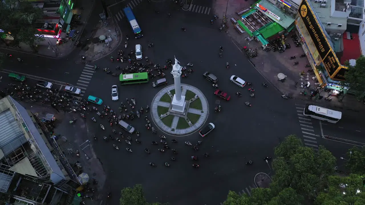 Traffic roundabout from drone flying towards center of intersection with large white monument with bus car and motorbike traffic