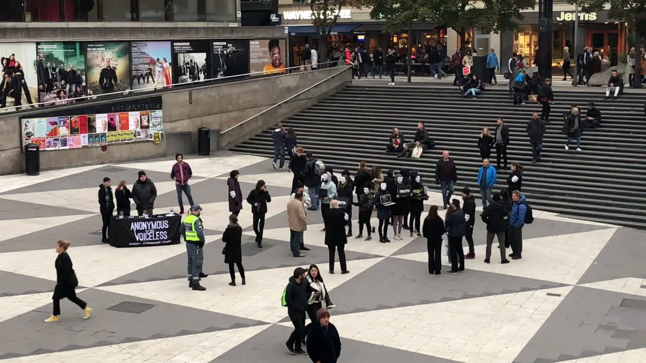 Anonymous demonstration protest in a shopping square of Stockholm Sweden with people walking by