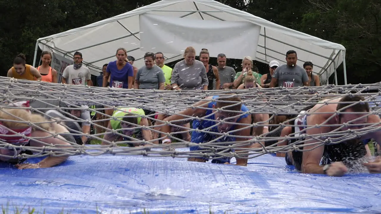 Mud Run Participants crawling under a cargo net slip and slide obstacle