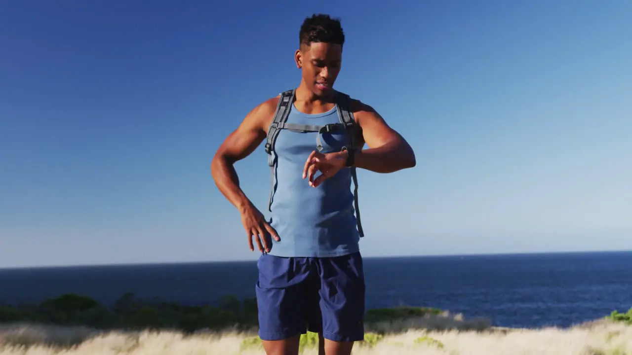 African american man cross country running using a smartwatch in countryside on a mountain