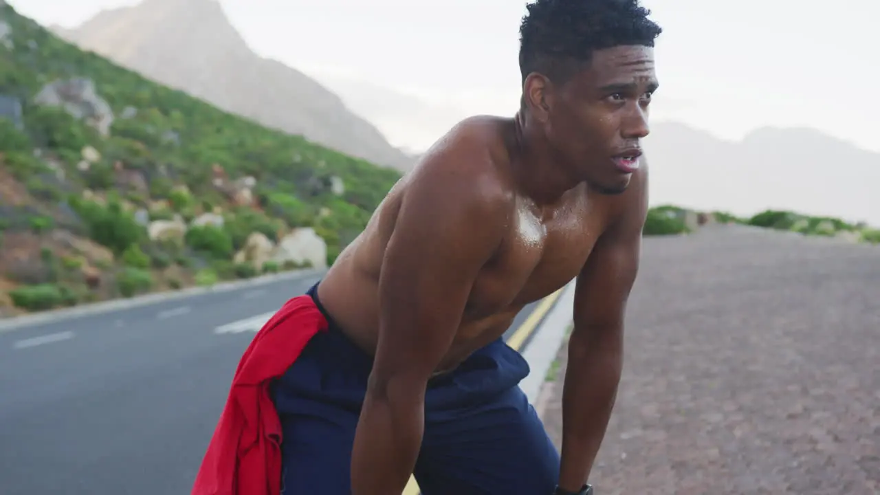 African american man exercising outdoors leaning on his knees on a coastal road