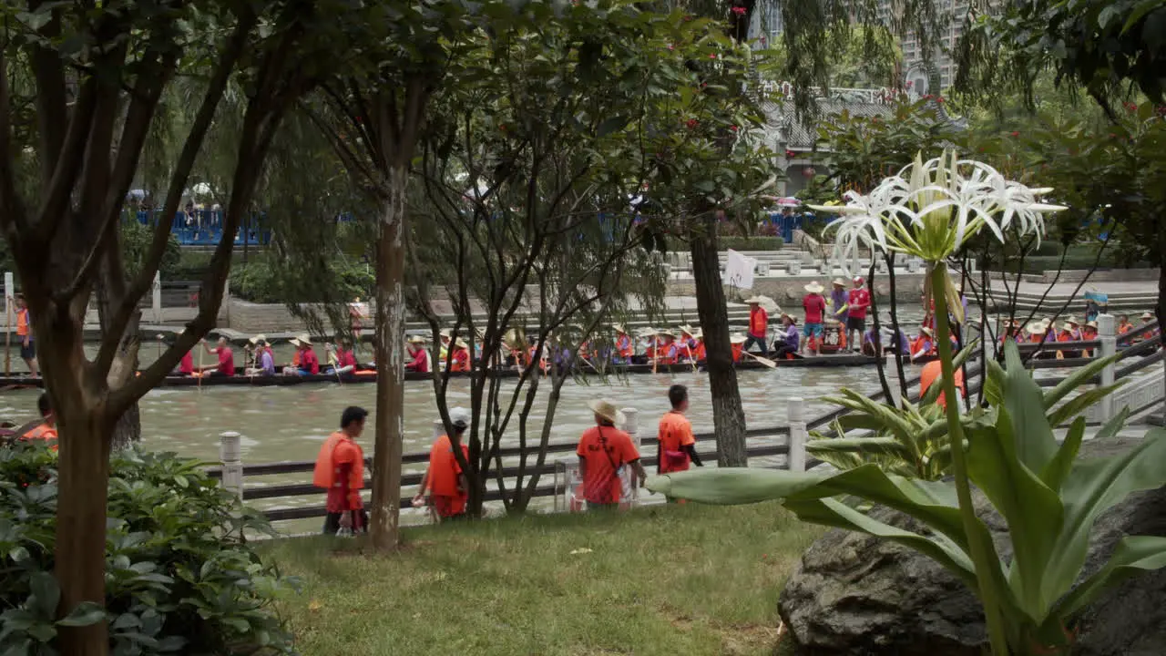 View from behind the trees of people paddling and hitting drums on a dragon boat during dragon boat festival in Guangzhou Guangdong China