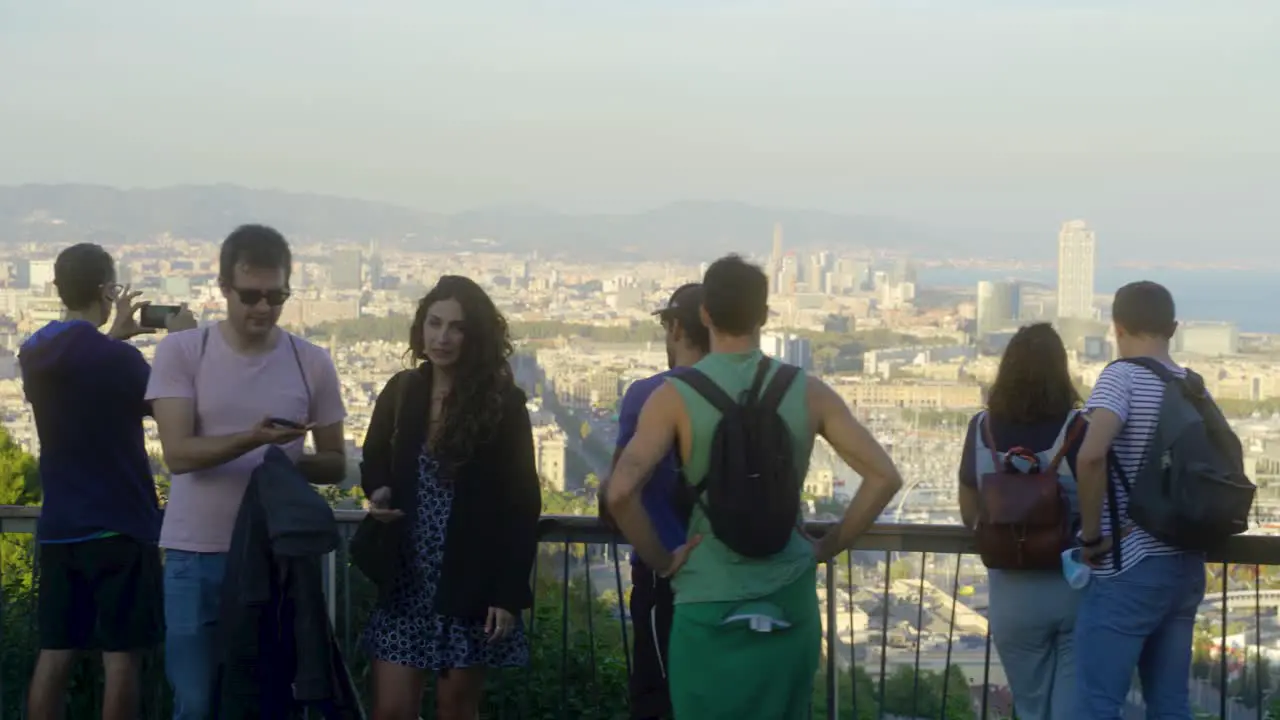 People on viewpoint overlooking city and harbor and taking photos with smartphone during sunset