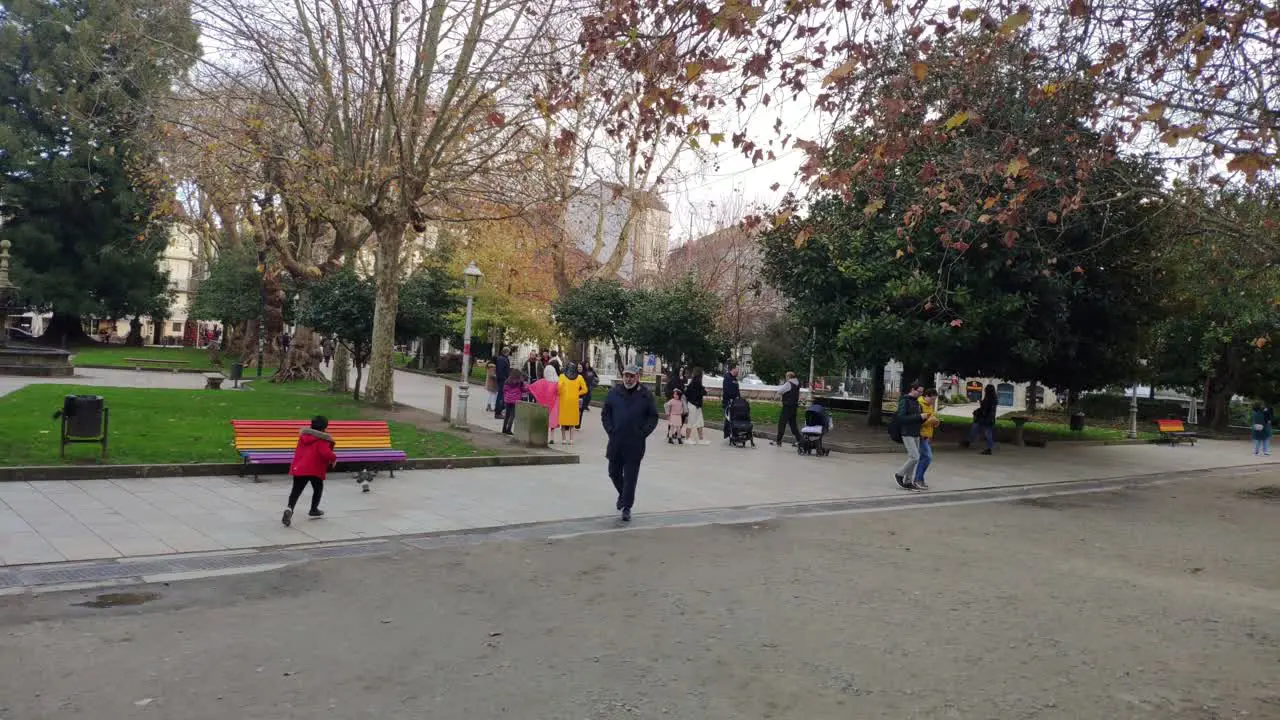 people walking quietly and socializing peacefully without altercations in city gardens with trees a child chasing a pigeon shot blocked Santiago de Compostela Galicia Spain