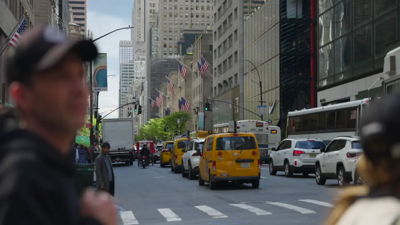 People waiting to cross crowded street of New York City with American flags and car traffic