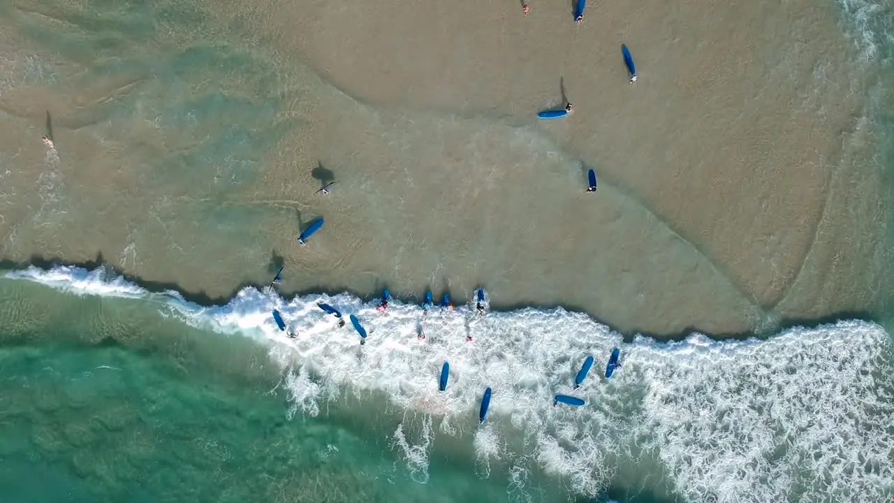 Aerial drone shot looking down on a large group of people learning to surf at the beach