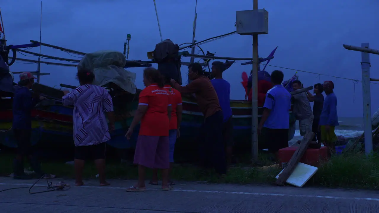 People protecting traditional wooden boat on the shore in heavy wind in Thailand