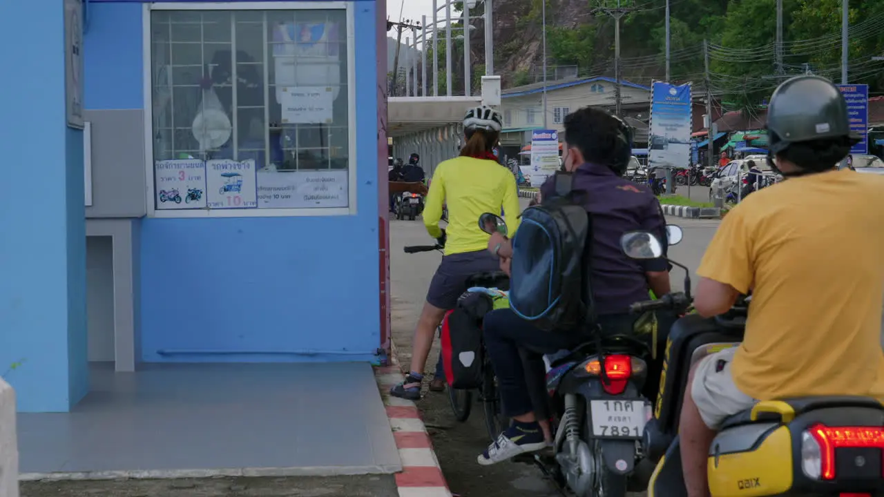 People on motorcycles and bikes paying toll to enter ferry boat in Thailand