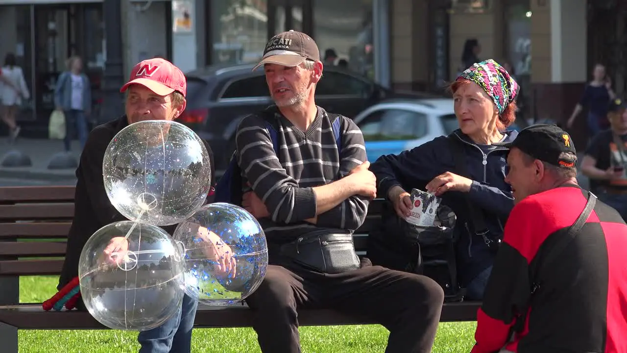 Ukrainians Sit On A Park Bench Enjoying The Sunshine In Central Lviv Ukraine