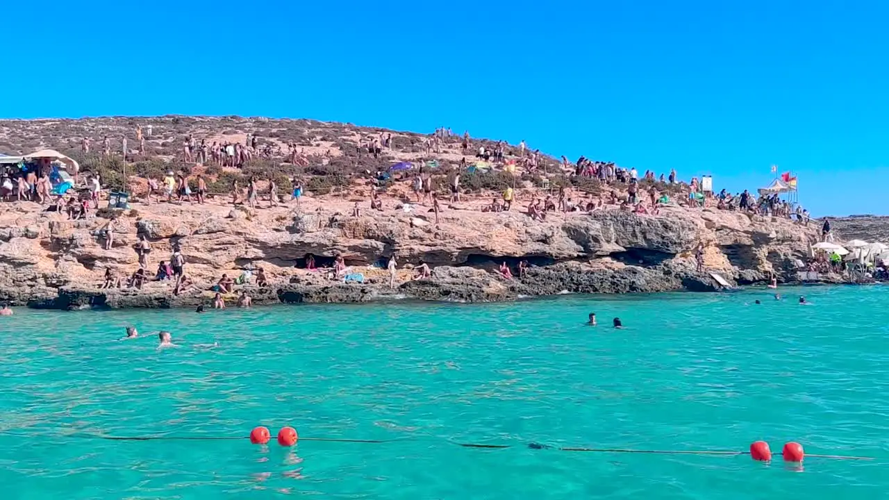 Panning shot from a touristic boat towards the rocky beach in Blue Lagoon Bay at Comino Island in Malta