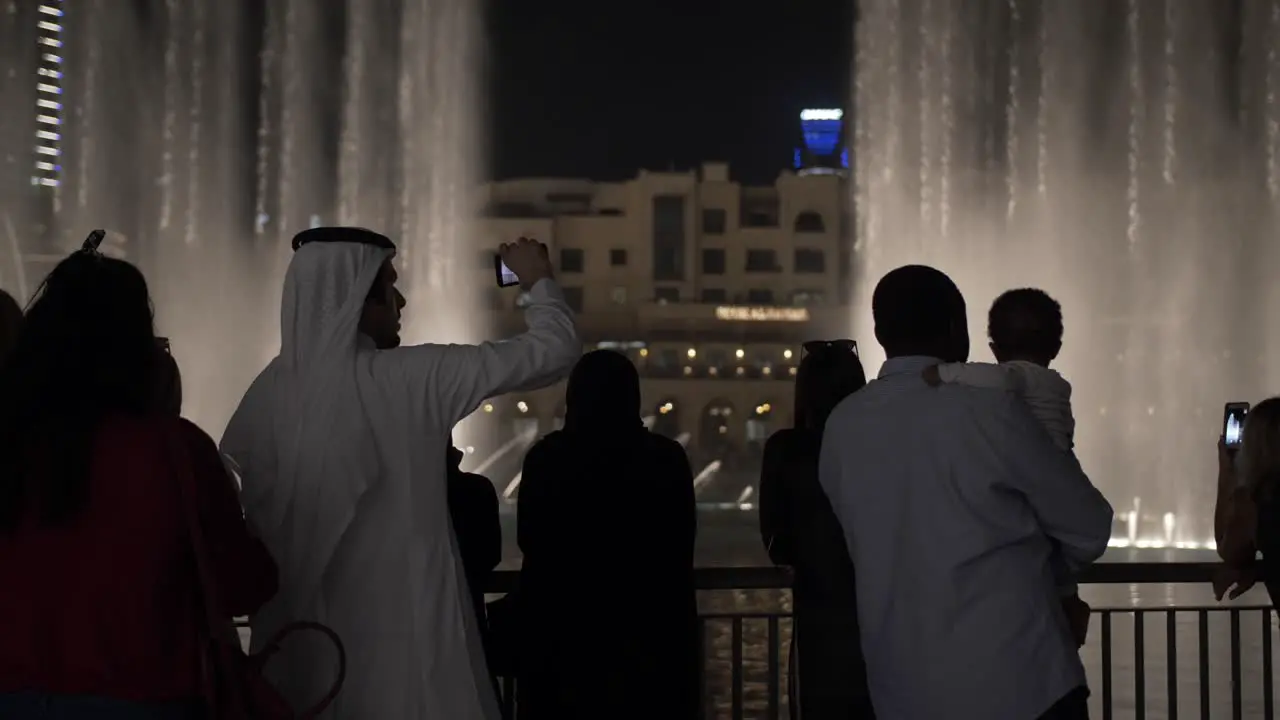 Middle eastern man and other people watching the water fountain light show at the Dubai mall