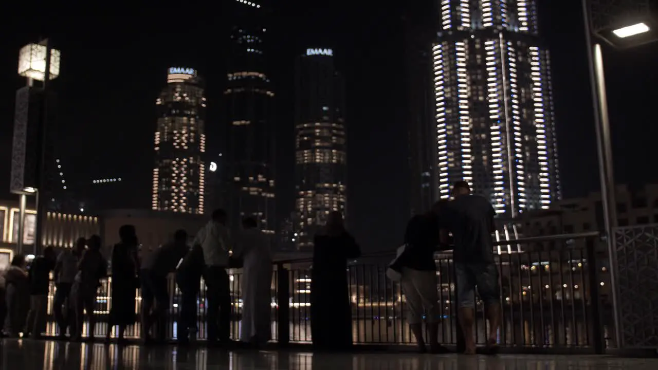 People watching the water fountain light show at the Dubai mall with distant lit up buildings and skyscrapers