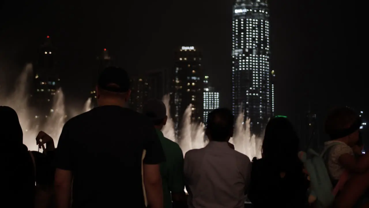 Crowd of people watching the water fountain light show at the Dubai mall with lit up skyscrapers in distance