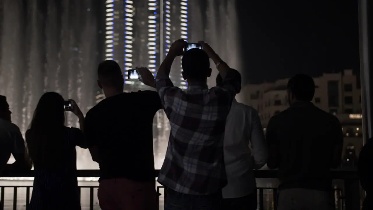 Tourists people watching the water fountain light show and taking pictures with phones at the Dubai mall