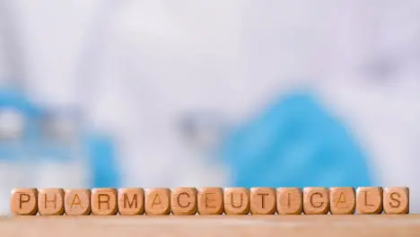 Medical Concept With Wooden Letter Cubes Or Dice Spelling Pharmaceuticals Against Background Of Scientist Working In Laboratory