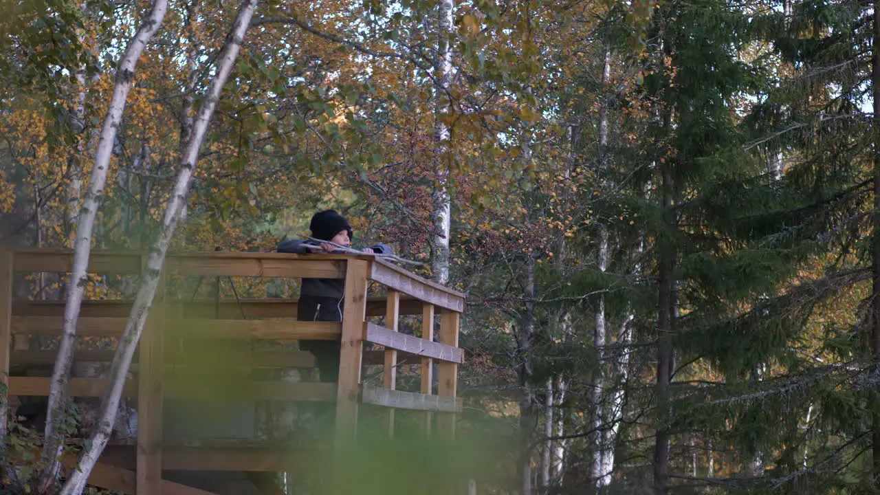 Camera moving through defocused leaves pointing at young boy enjoying autumn landscape view from lookout tower