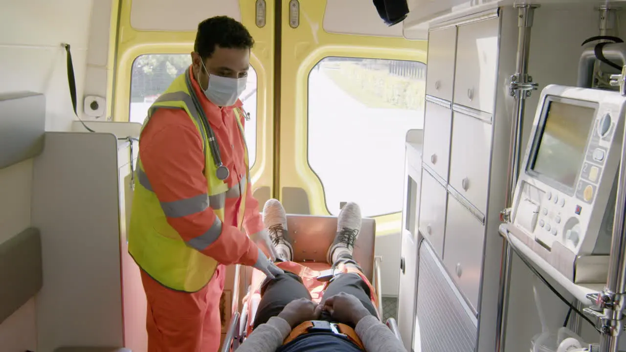 Paramedic Wearing Facial Mask Touching The Knee Of A Patient Lying On The Stretcher Inside An Ambulance