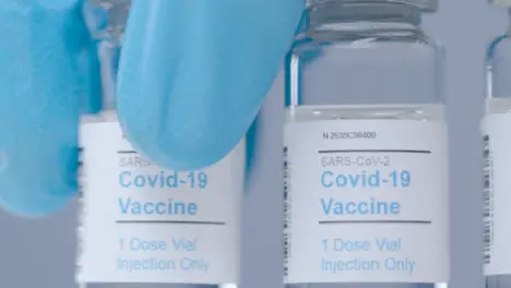 Sliding Extreme Close Up Shot Along Line of Covid Vaccine Vials As Hand Takes One Away