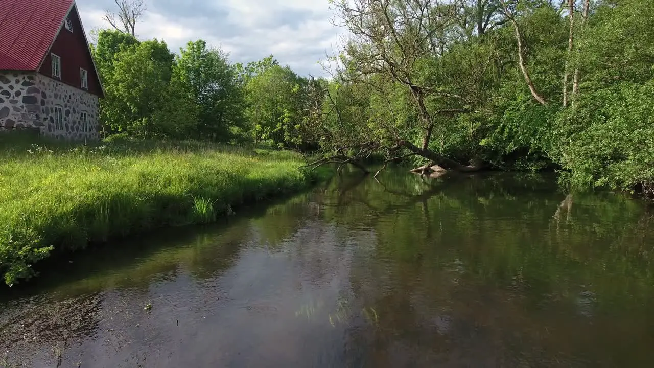 Low Branch By a Calm River Stream Next To an Old House in South Sweden Skåne Österlen Nybroån in Summertime Aerial Low Forward Slow