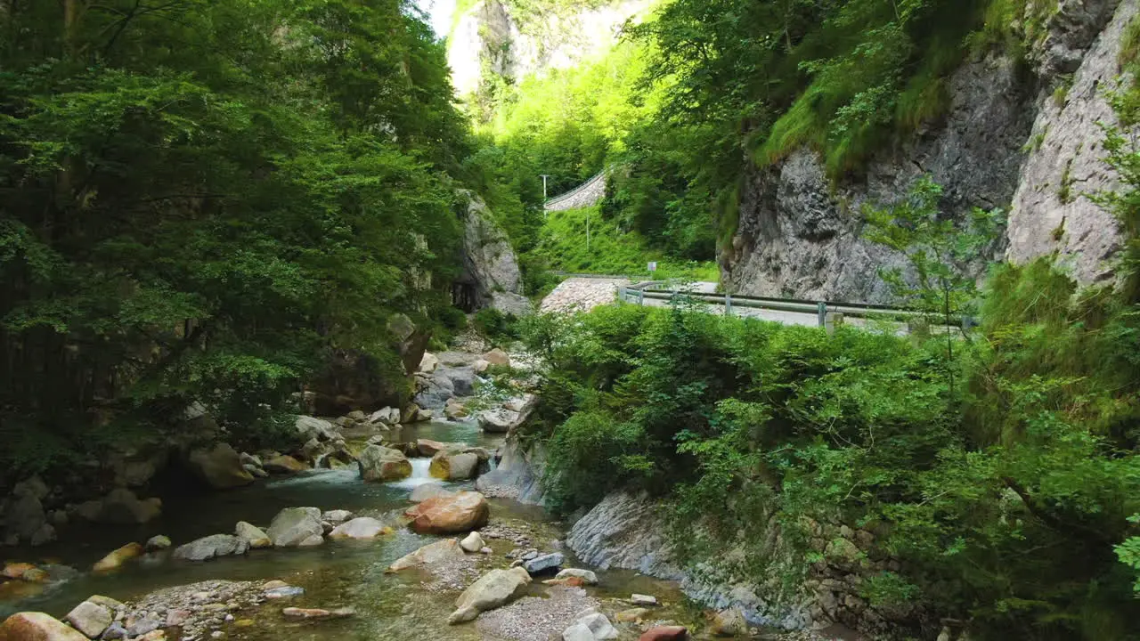 Clear shallow river with stones surrounded by rocks and trees by the traffic road