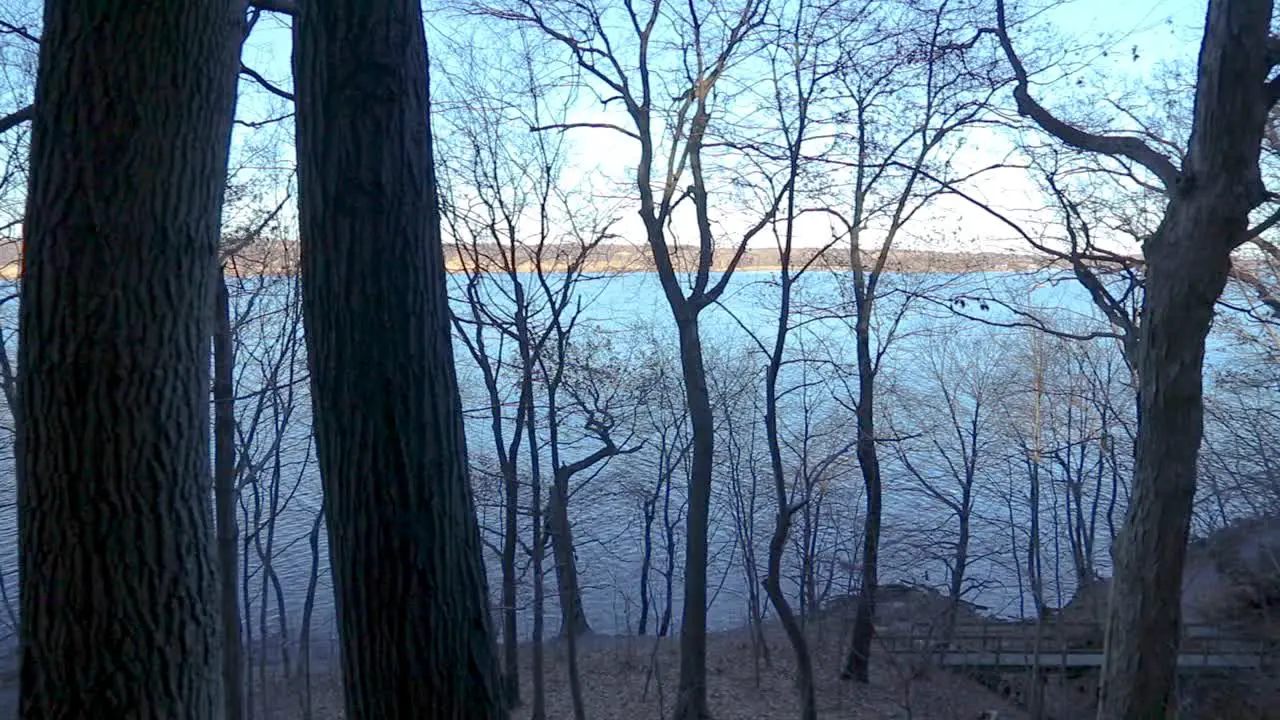 A horizontal pan from a higher vantage point of a river as seen through forest trees during a bright and sunny cloudless afternoon