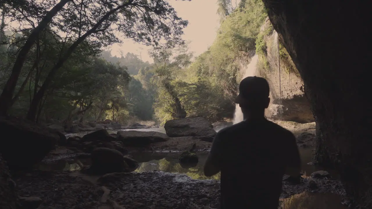 A young landscape and nature photographer taking pictures of a waterfall inside a dark cave in the middle of the rain forest