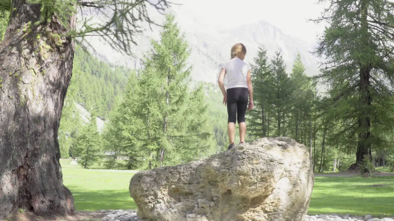 Little girl climbs on a rock and spreads her arms towards the mountain forest of Italian Alps 4K