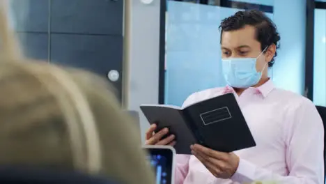 Over the Shoulder of Man In Face Mask Reading a Notebook