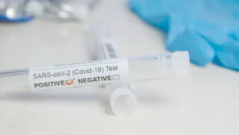 Sliding Close Up of COVID Positive Test Tube and Swab On a Table Surface