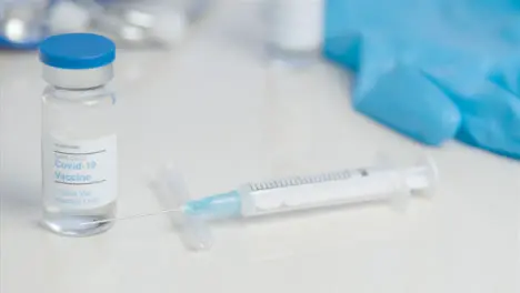 Sliding Close Up of COVID Vaccine Vial and Syringe On Table Surface