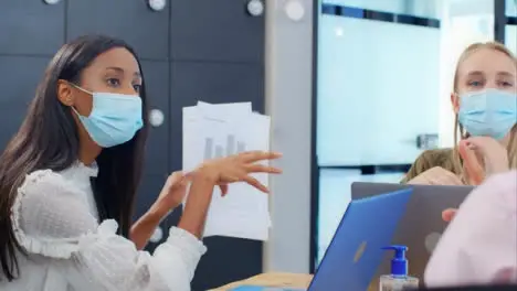 Over the Shoulder Pan of 3 Colleagues In Face Masks Discuss Documents