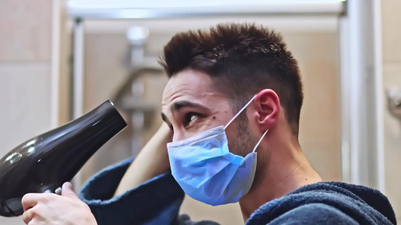 Man blow dry his hair in the bathroom wearing protective medical mask