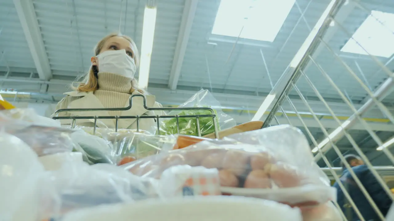 A Woman In A Protective Mask Walks With A Shopping Trolley At The Grocery Store