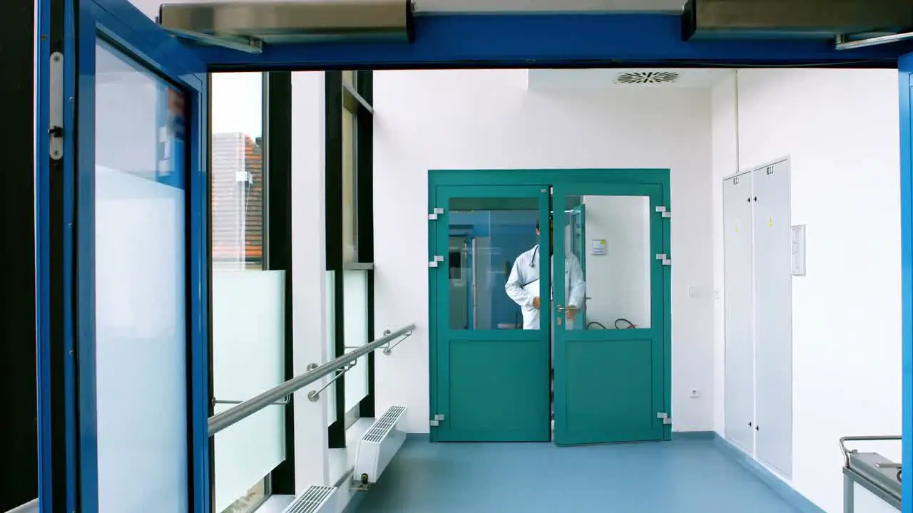 Male doctor holding a clipboard and walking in passageway of hospital