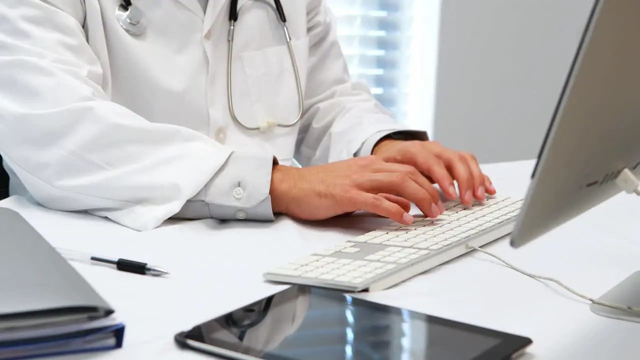 Mid-section of doctor typing on keyboard