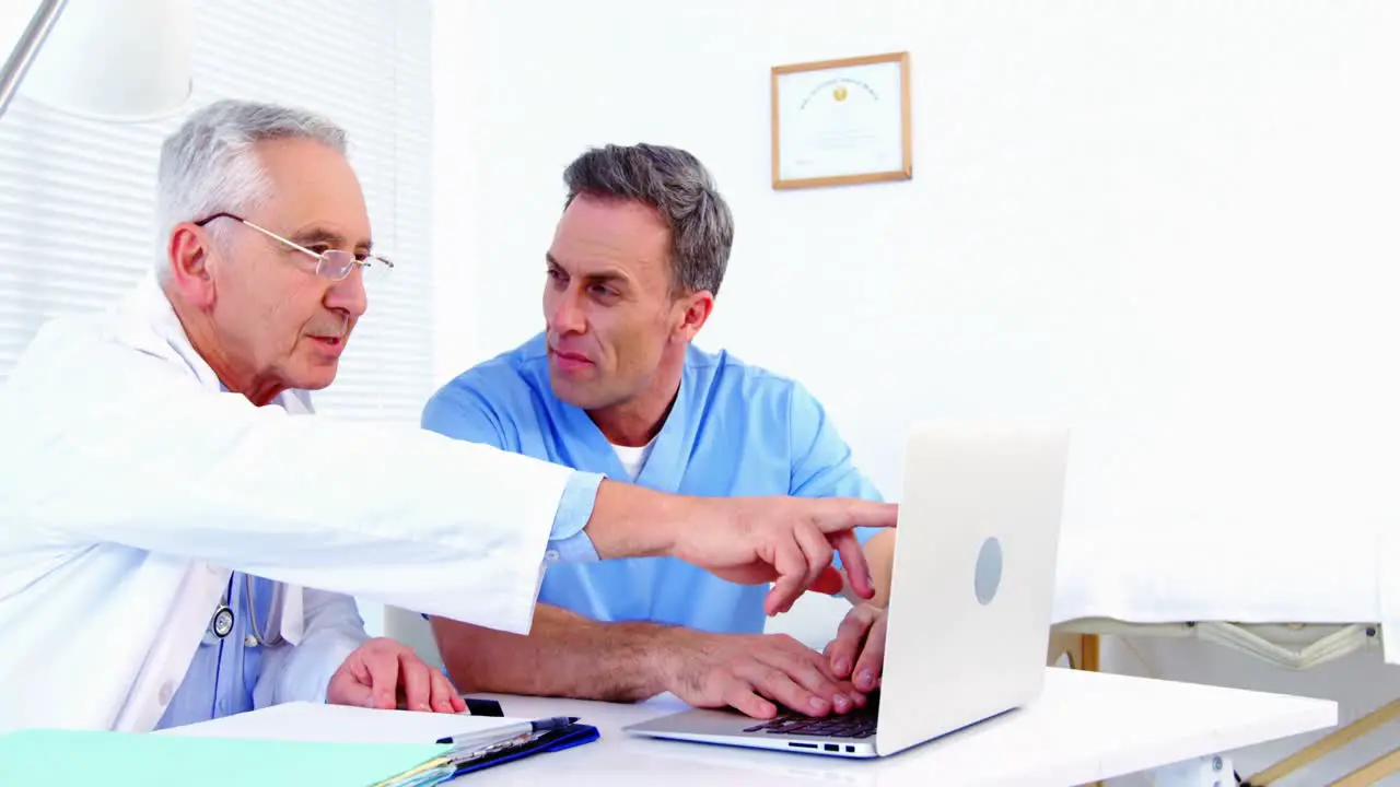 Male doctor and colleague discussing over laptop