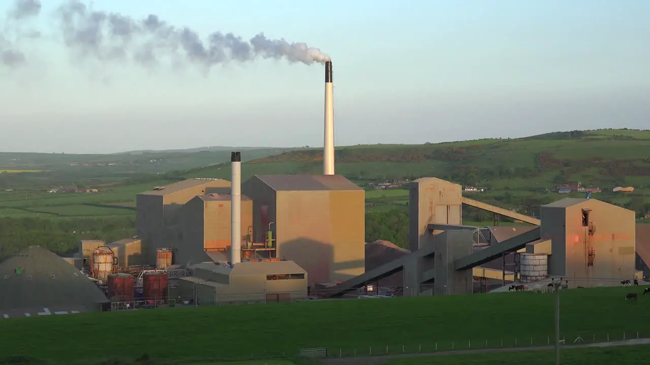 An industrial plant belching smoke in green rolling hills of England