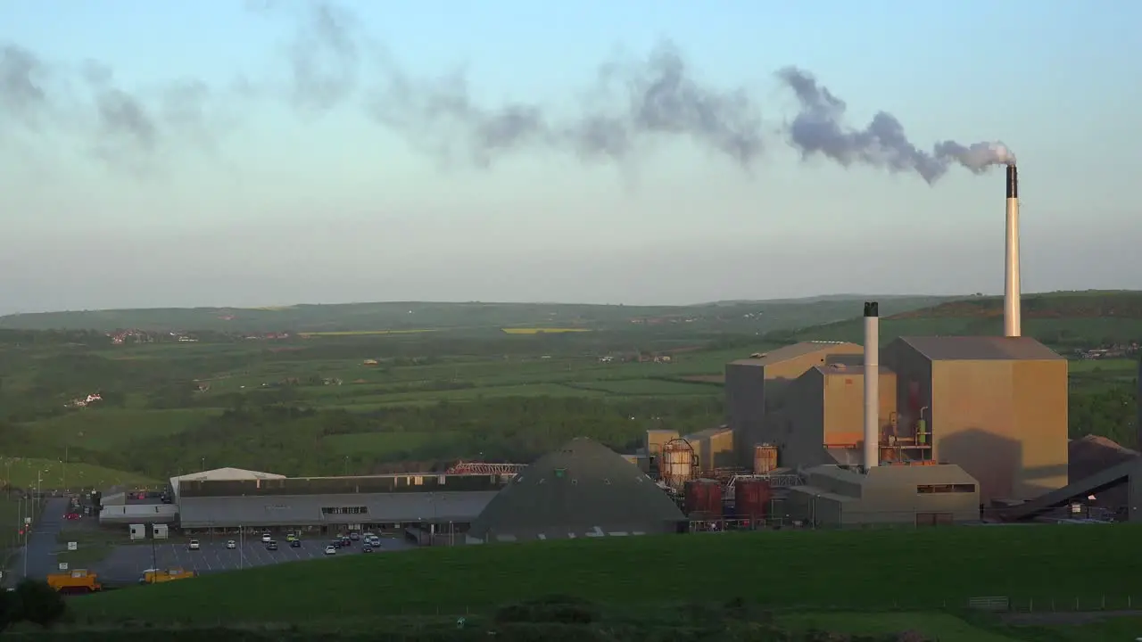 An industrial plant belching smoke in the green rolling hills of England