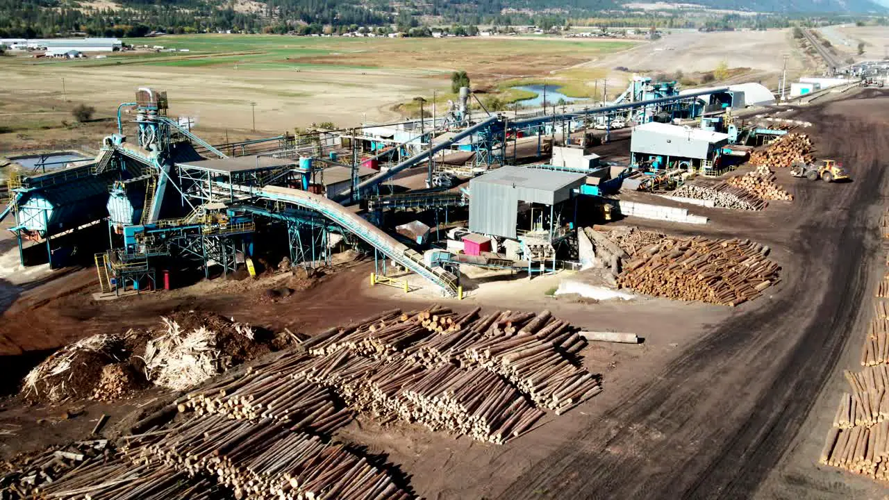 dolly forward zoom drone shot of a blue Sawmill Processing Plant with log piles in the background in a desert environment with heavy equipment moving