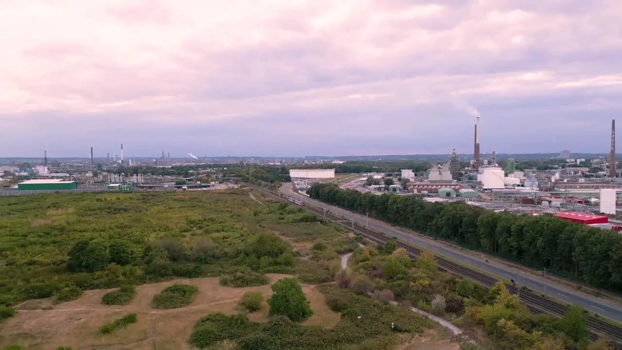 Fast flying drone towards an passenger tram on tracks to Sürth Cologne Germany aerial bird view of an chemical industry plant in the background and a little forest green zone in the front 2022