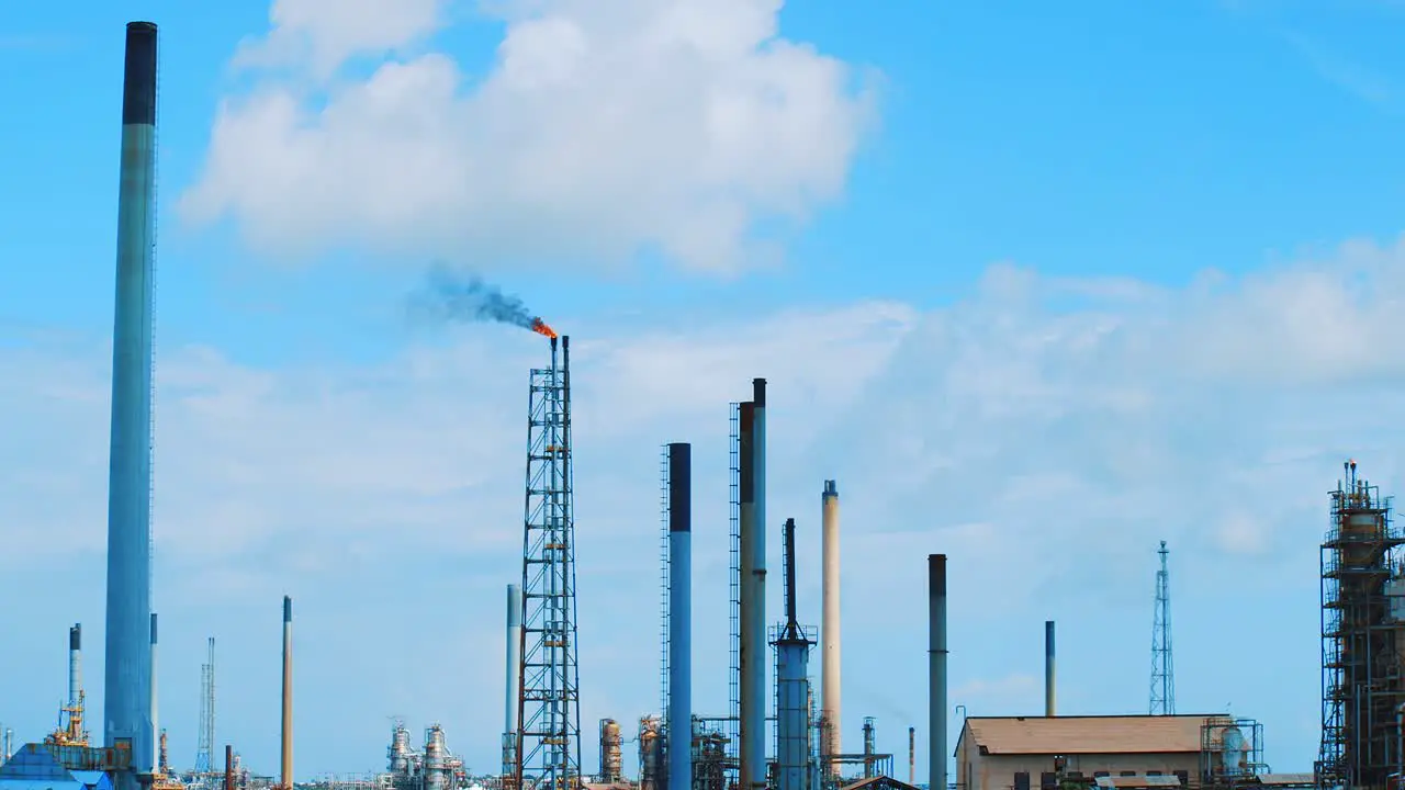 Slow motion wide angle shot of a large industrial refinery with black polluting smog pouring out into a clear blue sky in Curacao